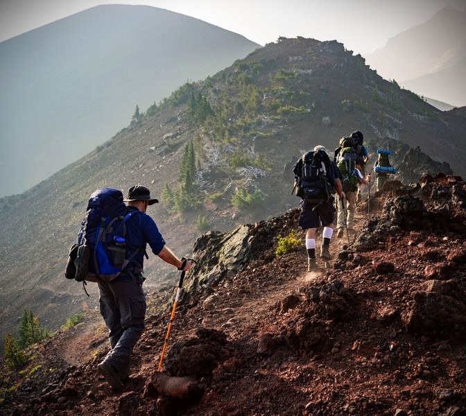 Group of hikers with backpacks ascending a rocky mountain ridge on a sunny day
